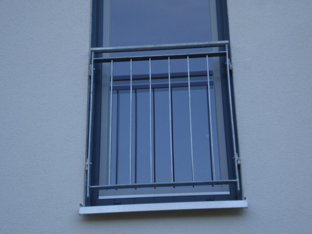 Verzinktes Geländer vor einem französischen Balkon an einer grauen Hausfassade