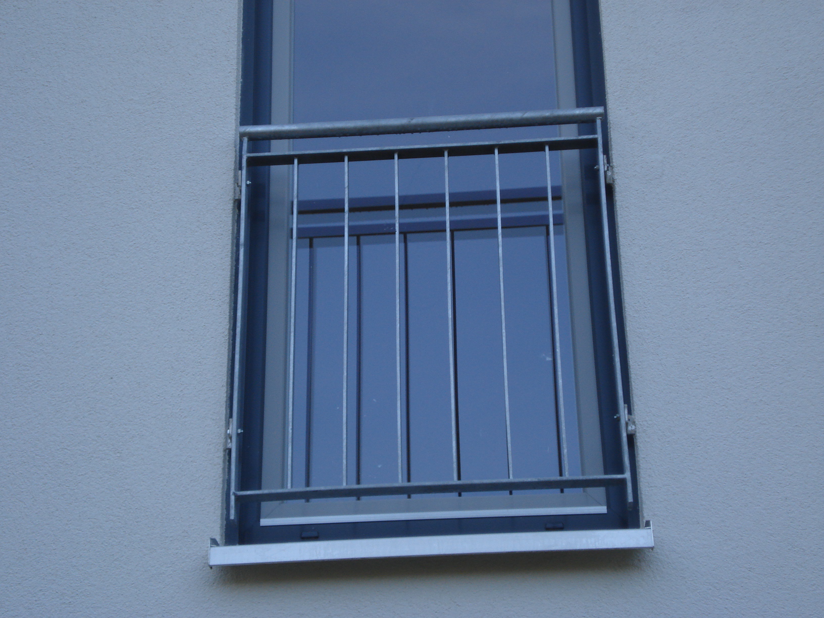 Verzinktes Geländer vor einem französischen Balkon an einer grauen Hausfassade