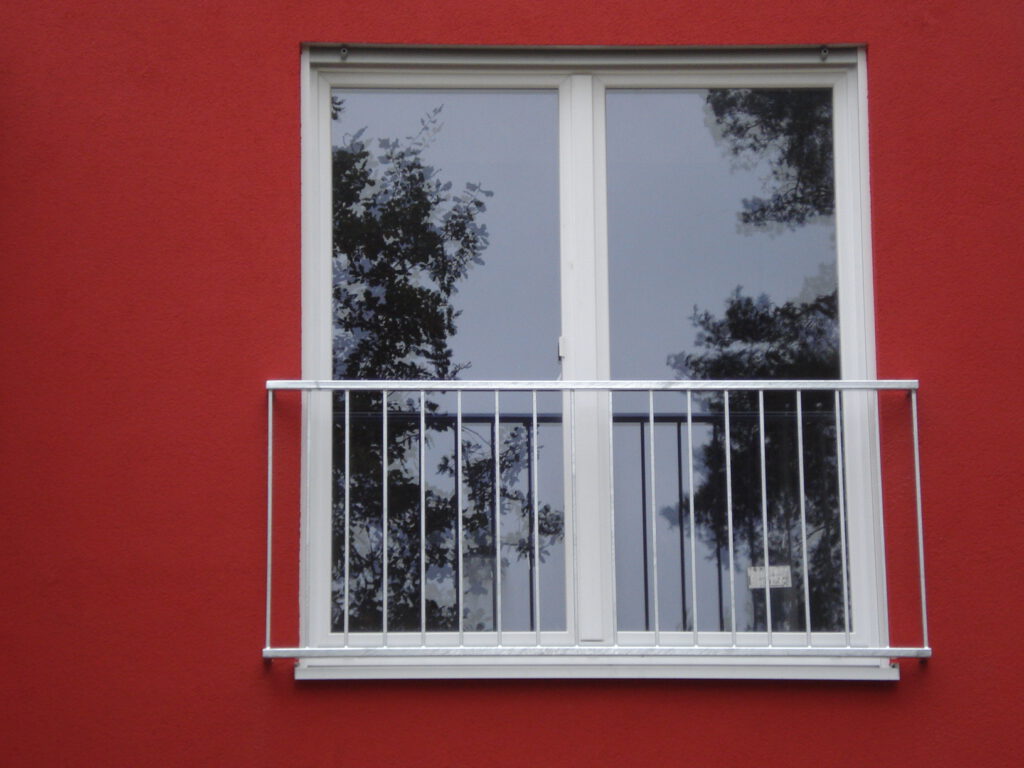 Verzinktes Geländer vor einem französischen Balkon an einer roten Hausfassade