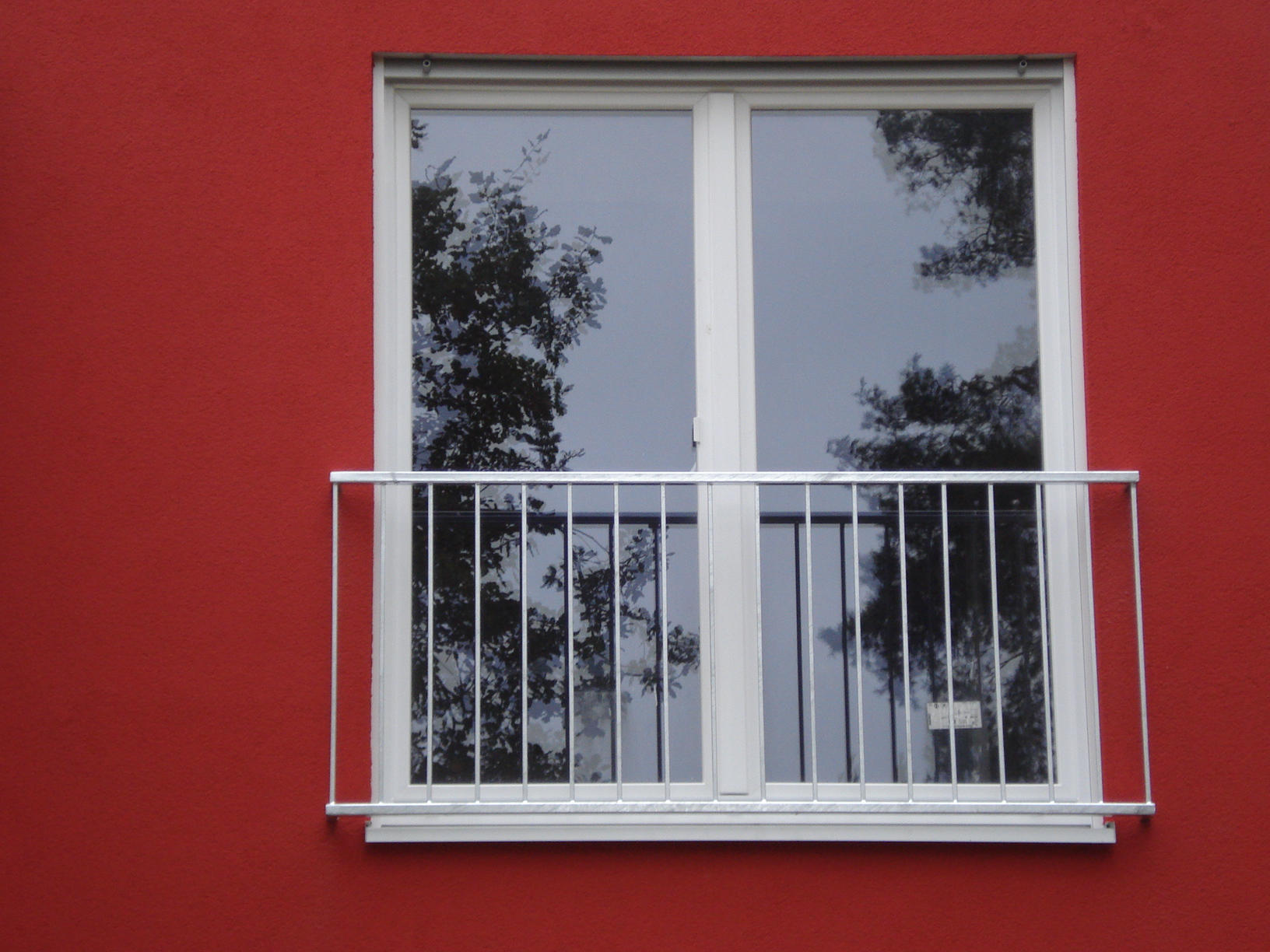 Verzinktes Geländer vor einem französischen Balkon an einer roten Hausfassade