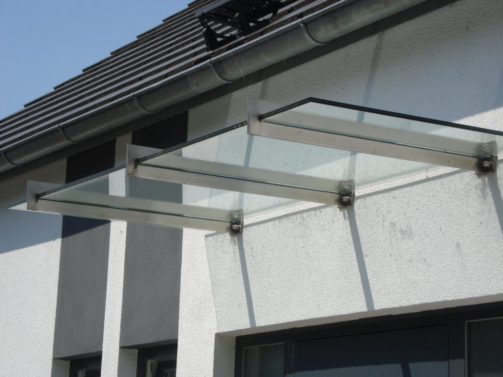 Glasvordach über einer Haustür mit Edelstahl-Halterungen an der Fassade