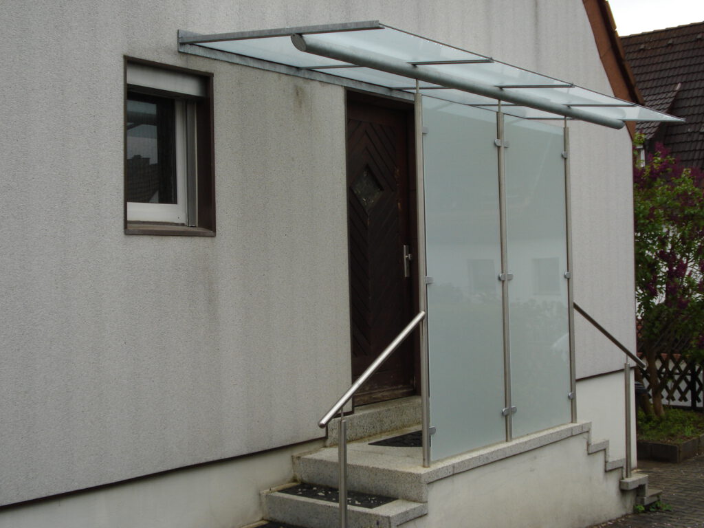Glasvordach mit seitlichem Windfang aus satiniertem Glas und Edelstahl-Handlauf an einer Haustür